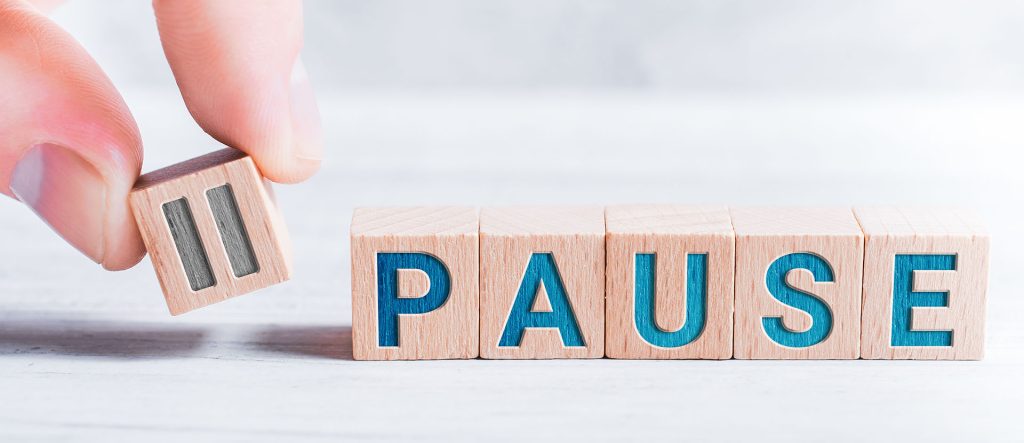 La palabra pausa formada por bloques de madera y dispuesta por dedos masculinos en una mesa blanca